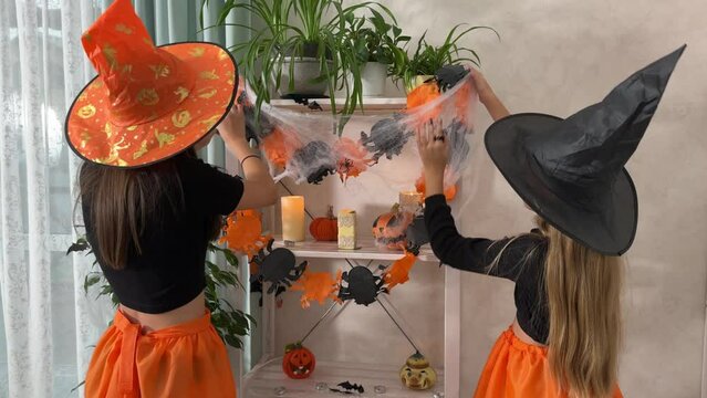 happy children in witch costumes are getting ready to celebrate Halloween, two girlfriends are decorating the room for Halloween