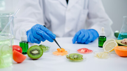 Female scientist is picking up a piece of orange to test and develop vitamin and quality of gel, oil, lotion or serum in laboratory. Fruits skin care, essence, moisturizer, medical, treatment product.