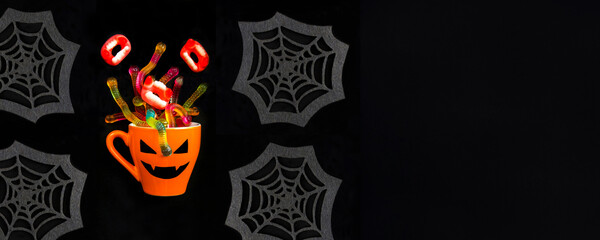 Orange cup with candy for Halloween on the black background. Copy space.