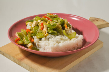 A plate of white rice with stir-fried oyong or luffa gourd and sliced yellow tofus on a wooden board isolated on a white background