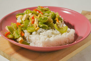 a plate of white rice with stir-fried oyong or luffa gourd and sliced yellow tofus on a wooden board isolated on a white background