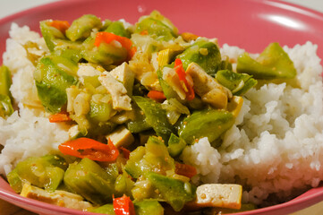 a plate of white rice with stir-fried oyong or luffa gourd and sliced yellow tofus on a wooden board isolated on a white background.