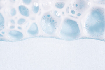 Foam texture on blue background, macro. Soap, shampoo, shower gel foam, face cleansing mousse or bubble mask sample. White cleanser foam bubbles on blue background.