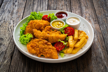 Seared breaded chicken nuggets with French fries and fresh vegetables on wooden table
