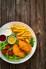 Seared breaded chicken nuggets with French fries and fresh vegetables on wooden table
