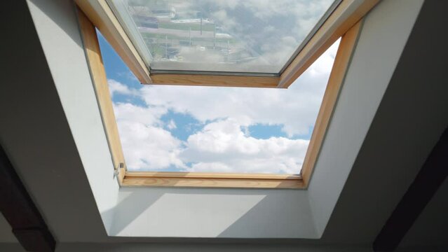 Looking on clouds flying past at the blue sky through open attic window in house roof