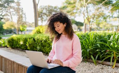 pretty curly young woman sitting in park working on laptop remote job