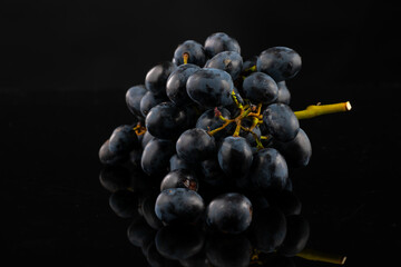 A bunch of dark blue grapes on a black background with highlights and reflection