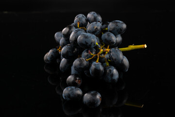 A bunch of dark blue grapes on a black background with highlights and reflection