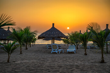 Sunset above Atlantic Ocean and a beach with palm trees, sunshades and sunbeds in Senegal, Africa