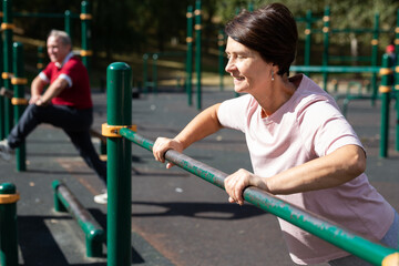 Mature woman doing push-ups from the crossbar on outdoor sports ground