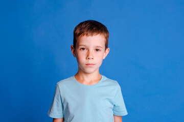 headshot serious boy in blue mockup T-shirt looking at camera on light blue studio background