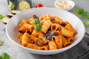 Pasta alla Norma. Italian pasta with eggplant, tomato sauce, cheese and basil in a gray concrete background. Comfort food.