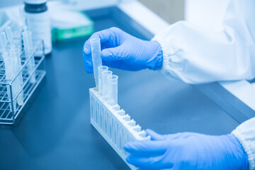 Close up scientist wearing blue gloves working with test tube in the flume hood at laboratory.Selective focus scientist hand holding sample blood test tube for fast laboratory at biochemistry unit.