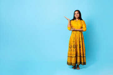 Fototapeta premium Indian Lady In Traditional Yellow Dress Showing Copy Space, Studio