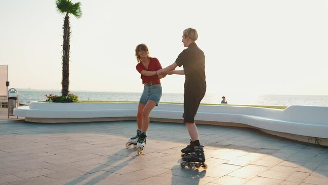 Lovely young couple holding hands while rollerblading on sunset by the sea