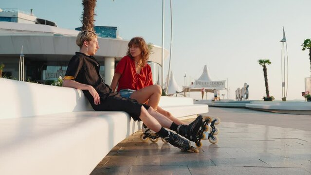 Smiling young couple talking after rollerblading on sunset by the sea