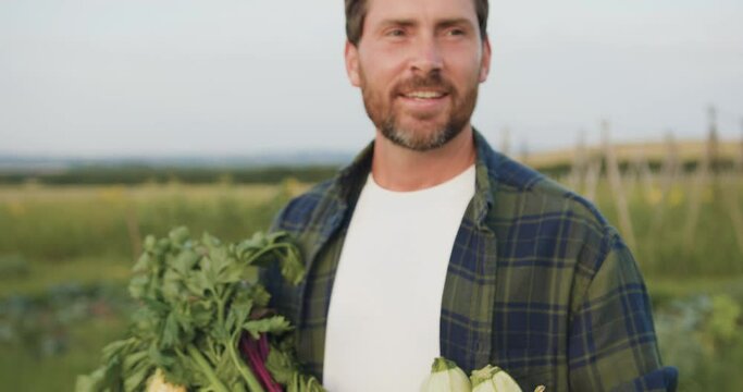 Close up. Happy smiling farmer man is holding box of organic vegetables look at camera at around sunlight agriculture farm field harvest garden nutrition organic fresh.
