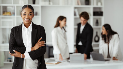 Happy black businesswoman posing with folded arms and smiling, posing during meeting with colleagues in office