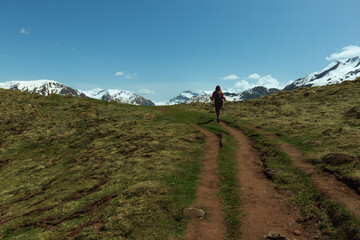 Woman walking on a route towards the Ibon de Estanes. With snowy background and green meadow.