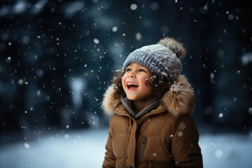 Cute child with happy face wearing a warm hat and warm jacket surrounded with snowflakes. Winter holidays concept.