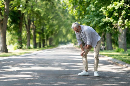 Mature Man Suffering Knee Injury While Walking Outdoors In Park