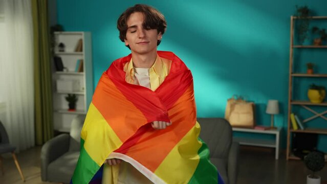 Medium video of a homosexual, bisexual, pansexual, transgener person looking at the camera and wrapping themselves in LGBT flag to encourage love, equality, freedom.