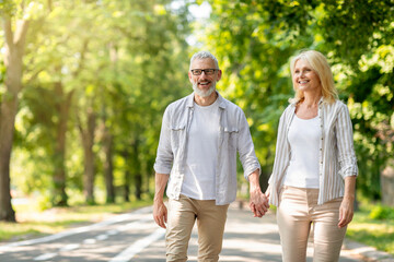 Happy mature man and woman holding hands and walking in park together