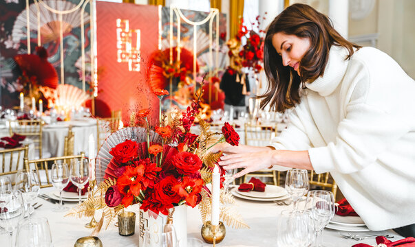 Red gold color flower decor for Chinese New Year celebration. Girl woman florist, decorator, organizer of events, parties, wedding planner making floral arrangement, festive bouquet, table decoration