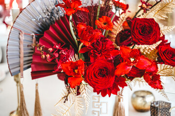 Obraz na płótnie Canvas Red gold golden color decor, floral arrangement. Festive bouquet, table decoration. Traditional Chinese New Year party restaurant celebration. Roses,poppies,fan,candles,tassels.Chinese lunar calendar