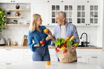 Healthy Eating. Happy senior spouses unpacking paper bags with groceries at home