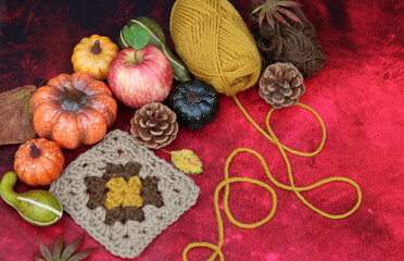 Autumn still life with pumpkins, apples and yarn on red background with copy space. Autumn crochet ideas. Cozy home concept. 