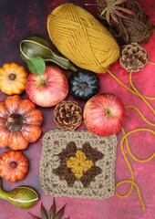 Obraz na płótnie Canvas Autumn crocheting. Top view photo of wool yarn balls, apples, squashes and leaves on red background with copy space. Coziness concept. 