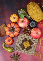 Autumn still life with pumpkins, apples and yarn on red background with copy space. Autumn crochet ideas. Cozy home concept. 
