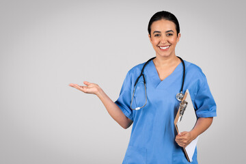 Cheerful latin woman doctor in blue workwear holding medical chart, pointing at empty space, showing ad or offer - obrazy, fototapety, plakaty