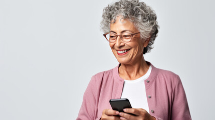 Fototapeta premium An elderly woman smiling and laughing with her phone against a colored background.