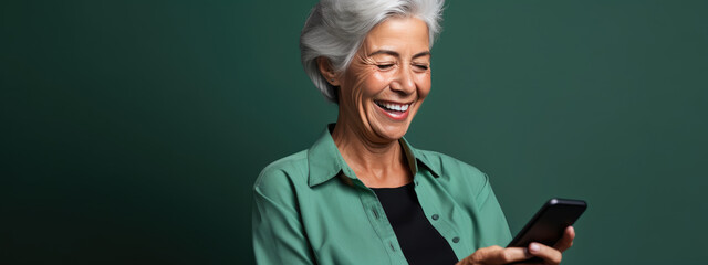 An elderly woman smiling and laughing with her phone against a colored background.