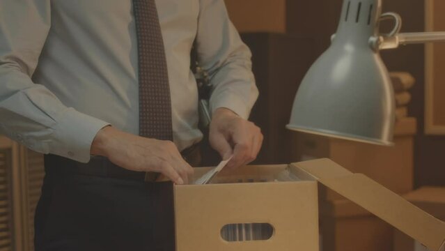 Cropped shot of unrecognizable police detective examining files in cardboard box with evidence while investigating criminal accident in office