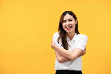 Young asian woman wearing white short sleeve shirt and smiling while embrace shoulders to hugging herself