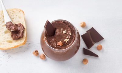 Vegan chocolate paste with banana and nuts surrounded by ingredients: chocolate and hazelnuts on a light gray background
