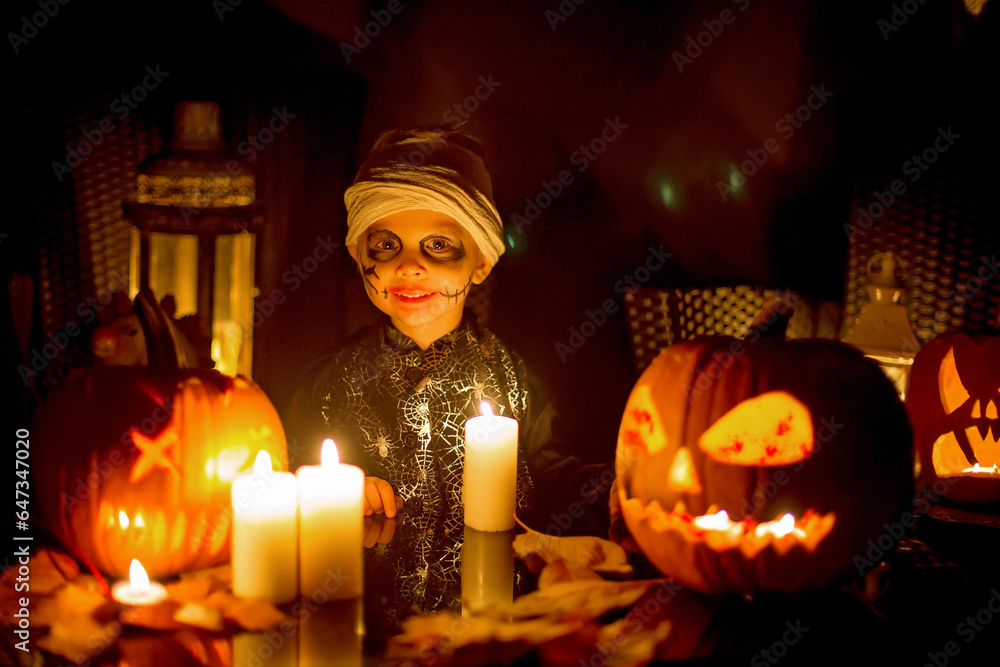 Wall mural Scary toddler child in halloween costume, playing with carved pumpkins