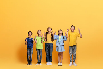 Naklejka premium Excited multiracial children pointing up at blank space, yellow background