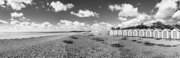 Colorfool beach huts on the shores of Littlehampton Long Beach in Sussex, England, UK; wooden huts on pebbles beach with clouded sky in black and white - obrazy, fototapety, plakaty