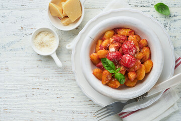 Potato gnocchi. Traditional homemade potato gnocchi with tomato sauce, basil and parmesan cheese on kitchen table on light grey kitchen table background. Traditional Italian food. Top view.
