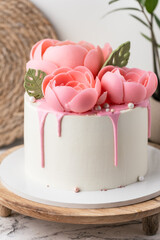 Birthday cake with white cream cheese frosting decorated with pink chocolate flowers on the wooden cake stand. Anniversary cake for a woman