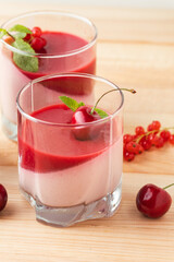 Delicious Italian dessert panna cotta with red berry sauce, fresh cherries, currant and mint leaves in a glass on the rustic wooden background.