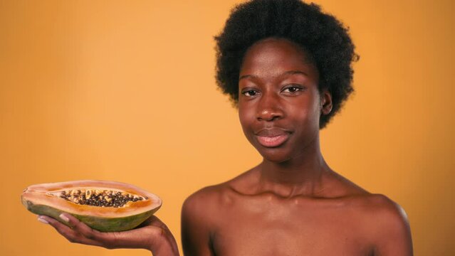 African American young woman with afro hair holding papaya in her hands isolated on orange background. Skin care and spa treatments.