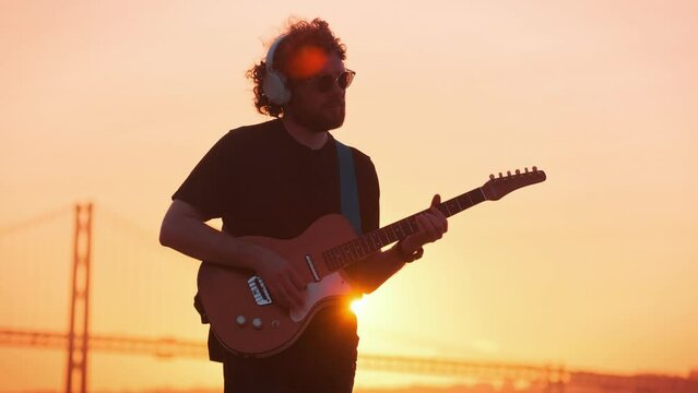 Hipster street musician in black playing electric guitar in street outdoors on sunset with lens flare