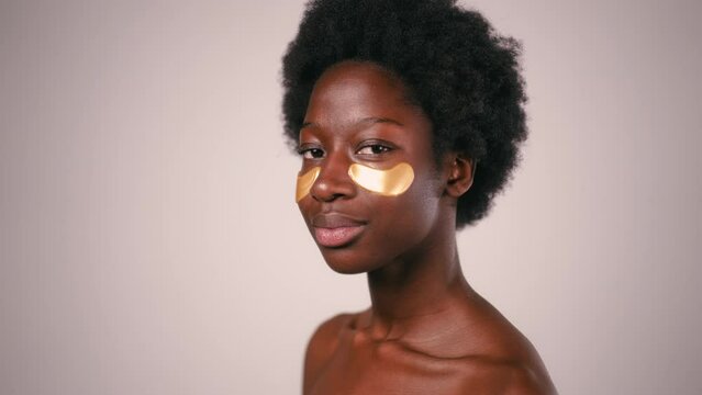 African American young woman with afro hair and perfect even healthy skin using eye patches isolated on gray background. Skin care and spa treatments.