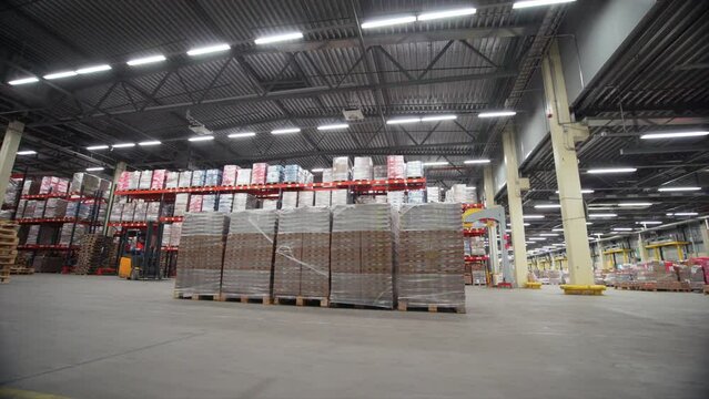 Forklift trucks move inside warehouse building. Creative. Large metal shelves at a modern warehouse and pallets with cardboard boxes.